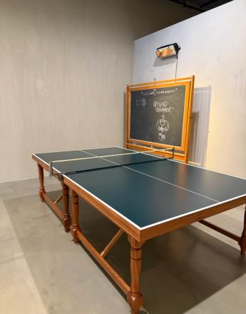 A dark green ping-pong table with a wooden frame in a room with a blackboard and a wall heater.