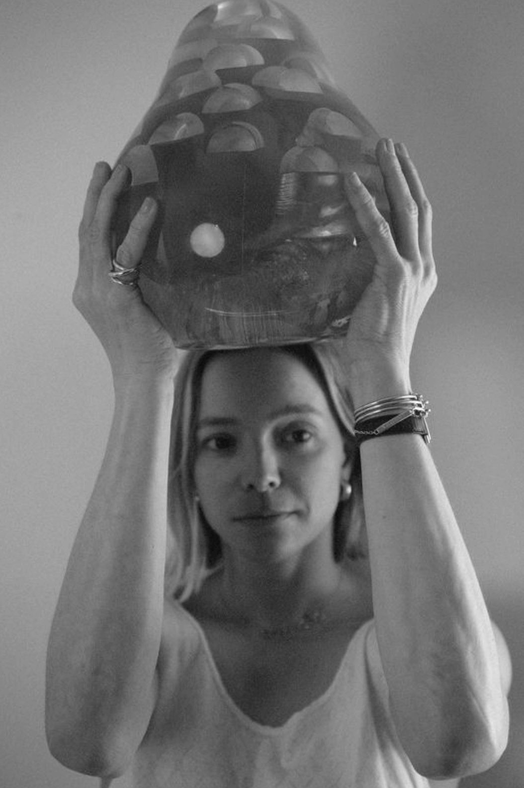 Black and white image of a woman holding a textured, mushroom-shaped object over her head.