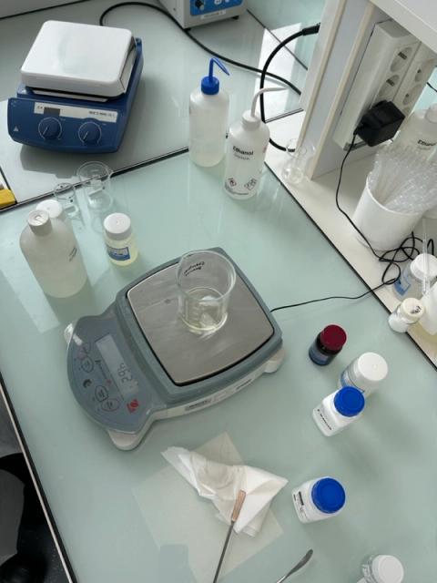 A lab bench with a digital scale displaying '46.2', beakers, chemical bottles, and a hot plate stirrer.
