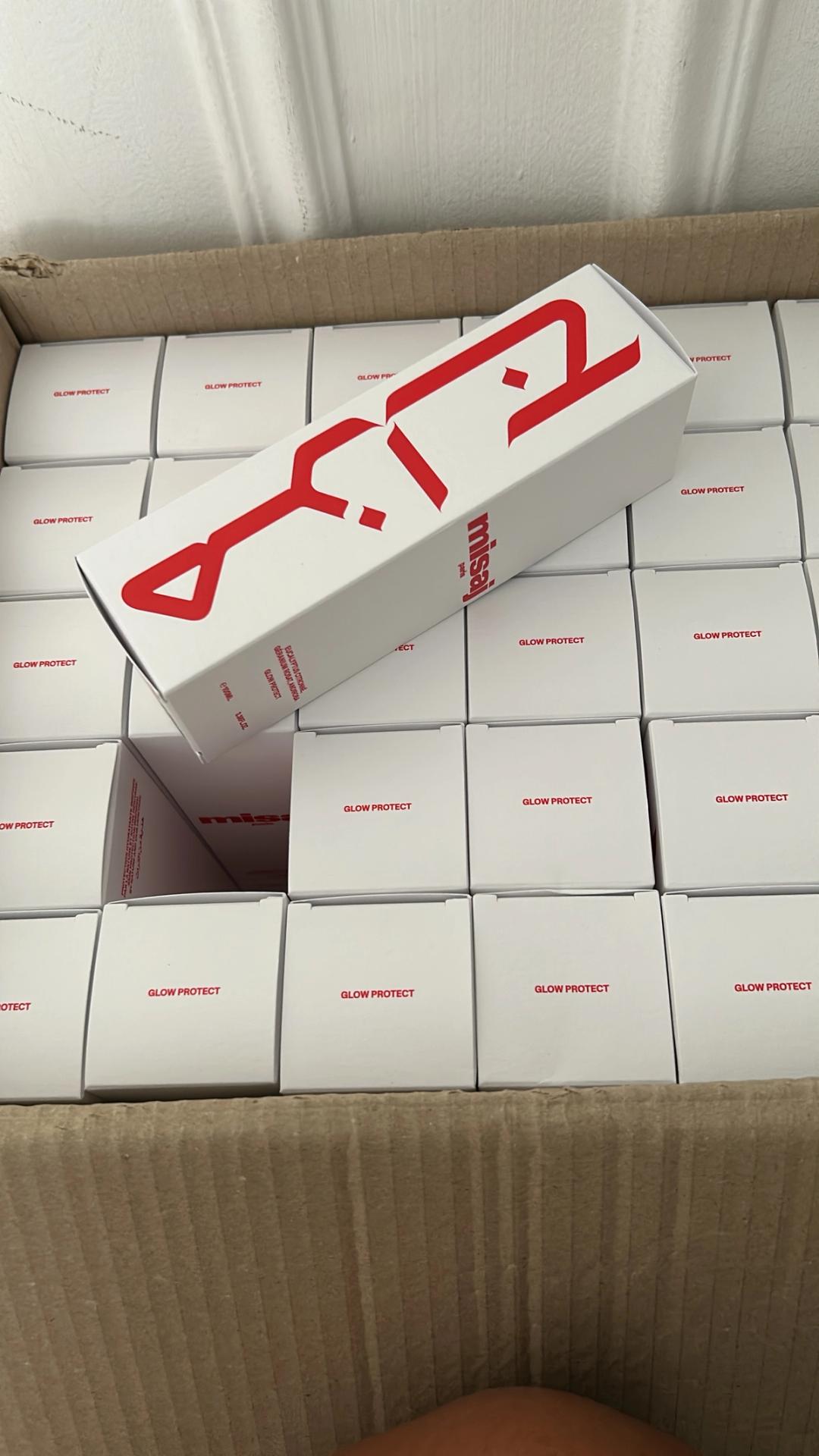 A cardboard box filled with white "Glow Protect" product boxes, with one larger box showing the "misal" brand tilted diagonally on top.