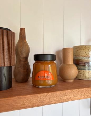 An "ACTIVIST" jar with orange contents sits on a wooden shelf surrounded by decorative wooden and ceramic objects.