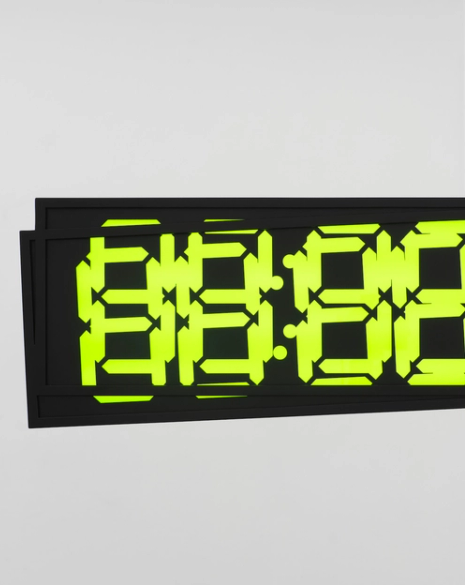 A digital clock showing "88:88" in bright green on a black screen, mounted on a white wall.