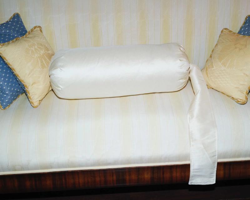 A light-striped sofa with an off-white bolster pillow with a ribbon, a cream patterned pillow, and a blue polka-dot pillow.
