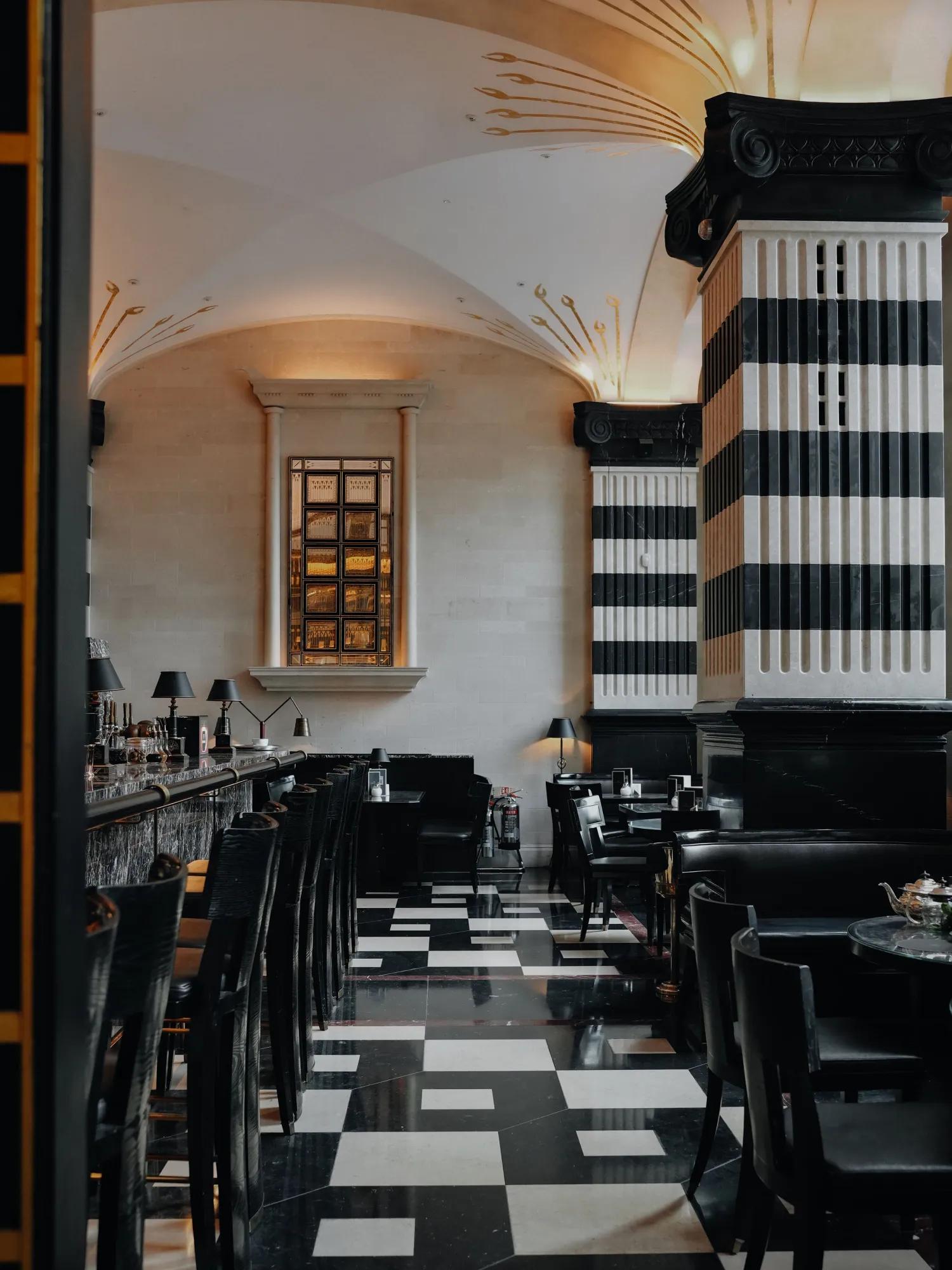 Elegant Art Deco bar interior with a black and white checkered floor, striped columns, and a vaulted ceiling with gold accents.