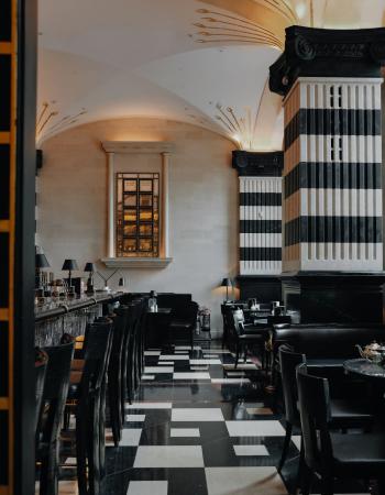 Elegant Art Deco bar interior with a black and white checkered floor, striped columns, and a vaulted ceiling with gold accents.