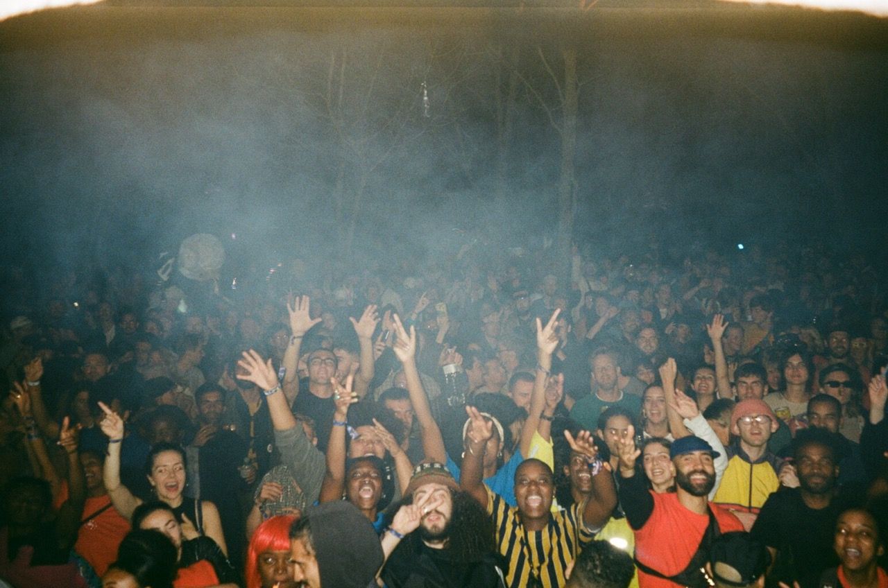 A large, diverse crowd raises their hands at a smoky outdoor night event.