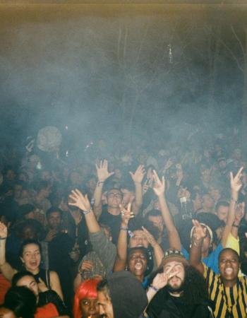 A large, diverse crowd raises their hands at a smoky outdoor night event.