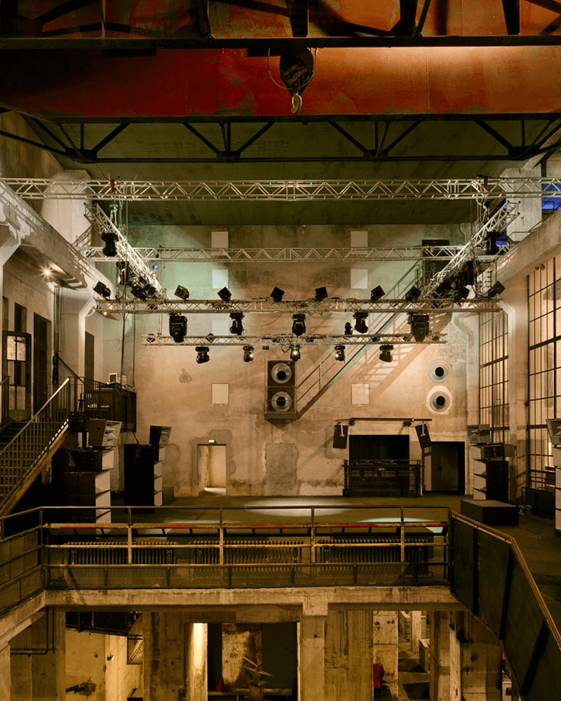 An empty, multi-level industrial event venue with a large lighting rig and sound system.