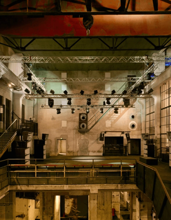 An empty, multi-level industrial event venue with a large lighting rig and sound system.