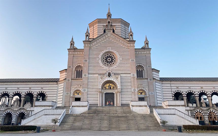 A grand, horizontally striped stone building with a central rose window, ornate entrance, wide stairs, and symmetrical arched wings.