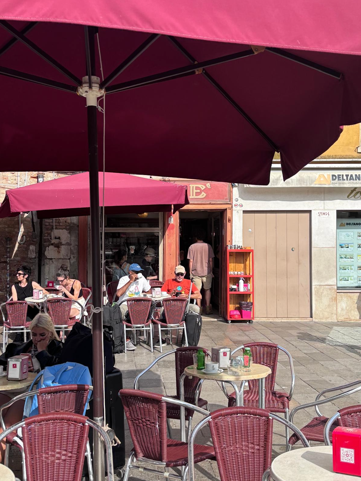 An outdoor cafe with people sitting at tables under large red umbrellas.
