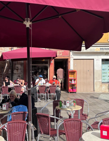 An outdoor cafe with people sitting at tables under large red umbrellas.