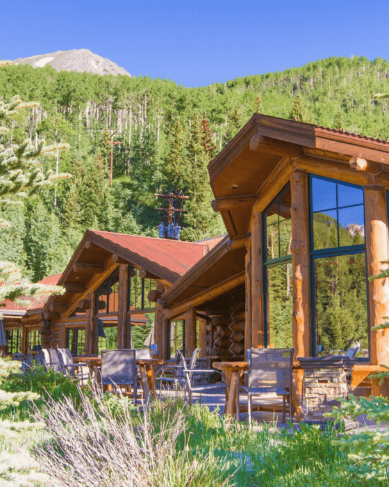 Rustic log cabins with outdoor patio seating in front of a forested mountain.