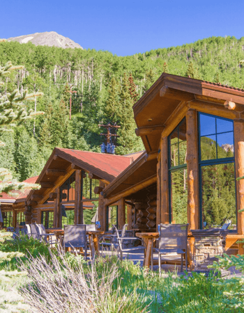 Rustic log cabins with outdoor patio seating in front of a forested mountain.