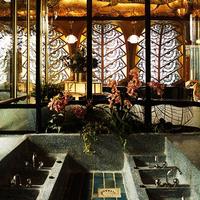 An ornate Art Deco interior featuring a large multi-basin stone sink, intricate geometric stained-glass windows, and a lotus-petal ceiling light.