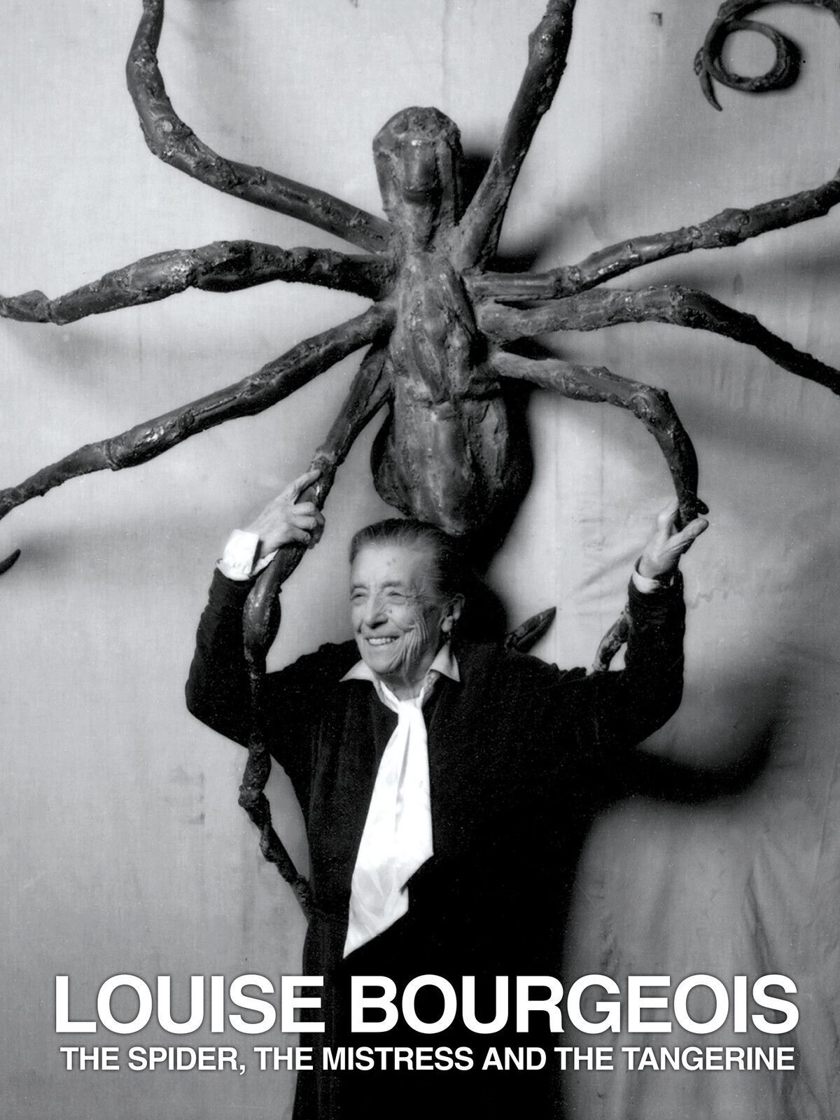 Black and white photo of artist Louise Bourgeois smiling and holding a large spider sculpture above her head. Text reads: 'LOUISE BOURGEOIS THE SPIDER, THE MISTRESS AND THE TANGERINE'.