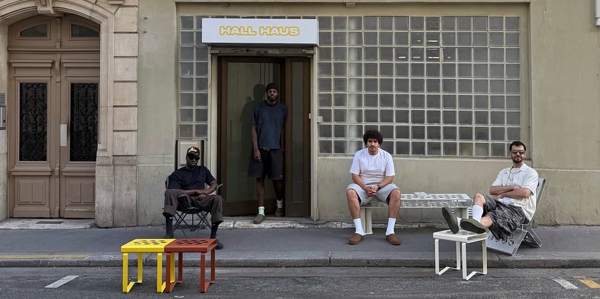 Four men in a white room displaying modular yellow panels and colorful perforated chairs.