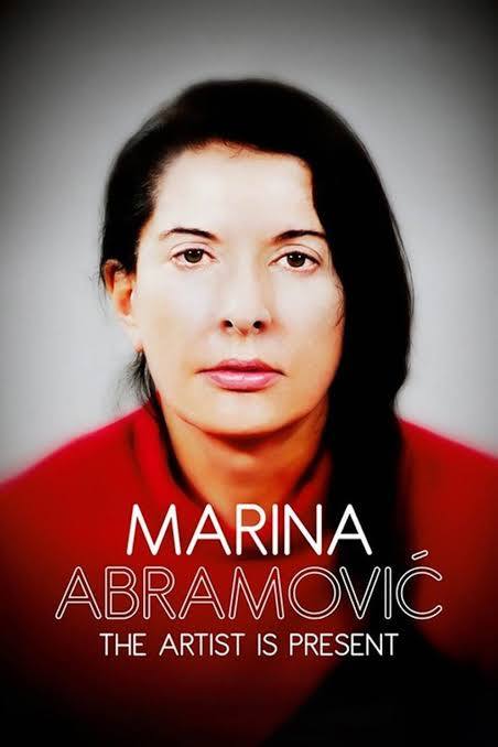 A woman with dark hair and a serious expression, wearing a red top, looks directly forward. Text below reads "MARINA ABRAMOVIĆ THE ARTIST IS PRESENT."