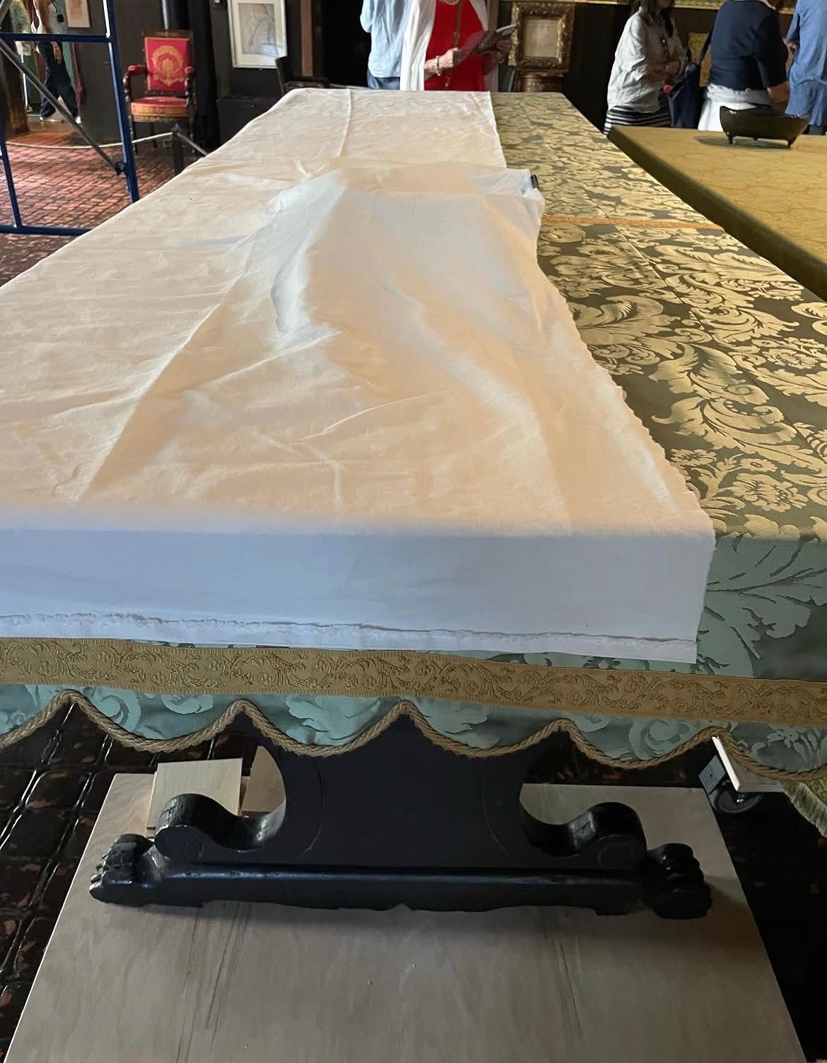A long table covered partially in white fabric and partially in green patterned fabric, with a decorative black stand in the foreground.