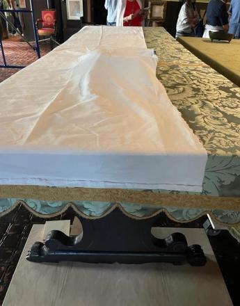 A long table covered partially in white fabric and partially in green patterned fabric, with a decorative black stand in the foreground.