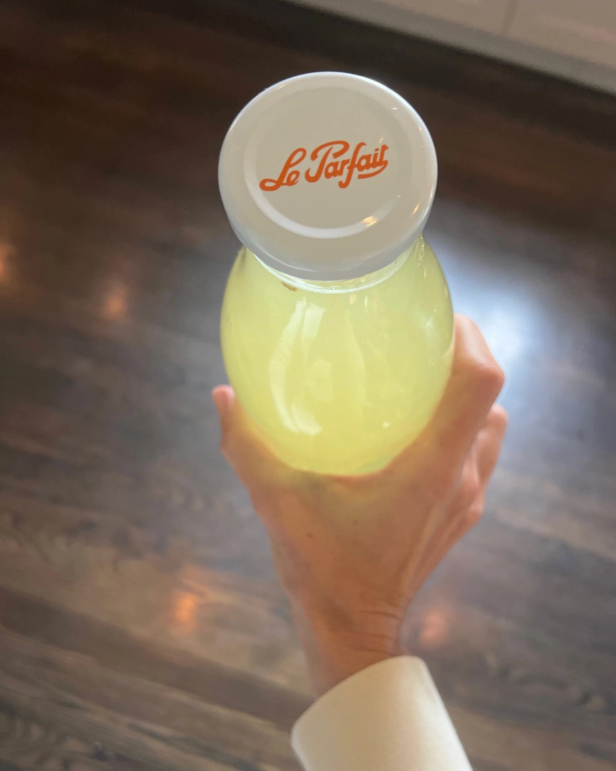 Hand holding a bottle of yellow liquid with a white "Le Parfait" cap.