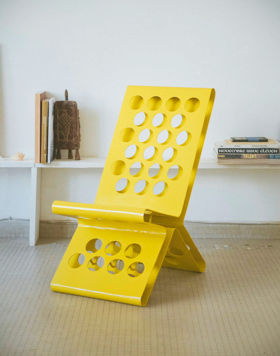 A vibrant yellow contemporary lounge chair with multiple circular cutouts, set against a white wall.