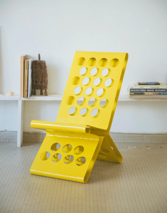 A vibrant yellow contemporary lounge chair with multiple circular cutouts, set against a white wall.