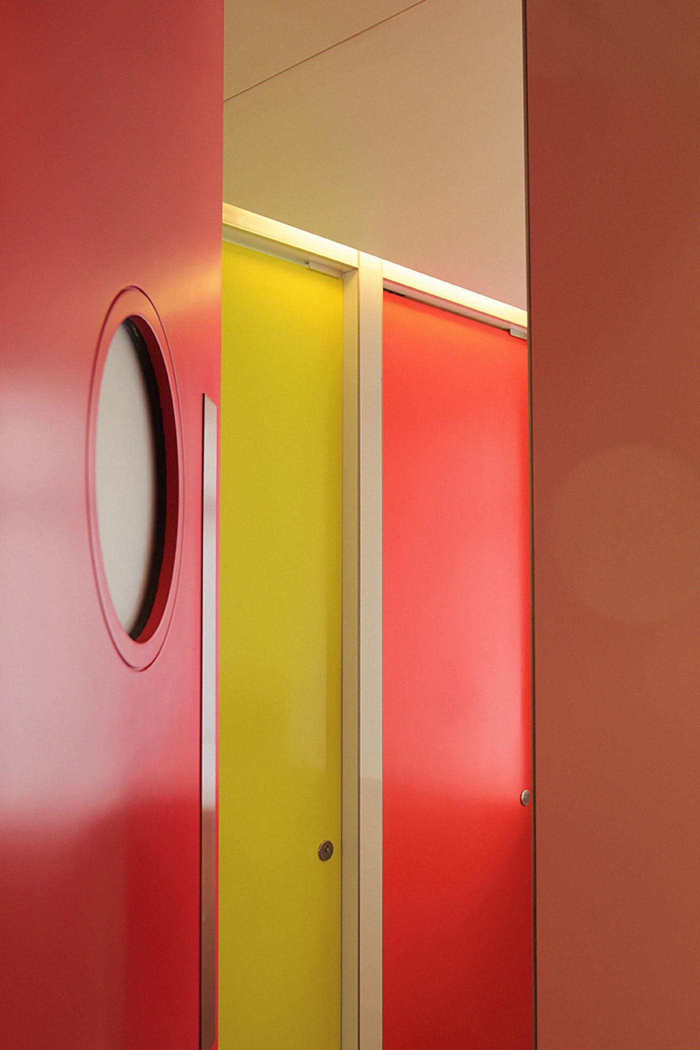 A modern interior with a red door featuring an oval window, a yellow door, and another red door.
