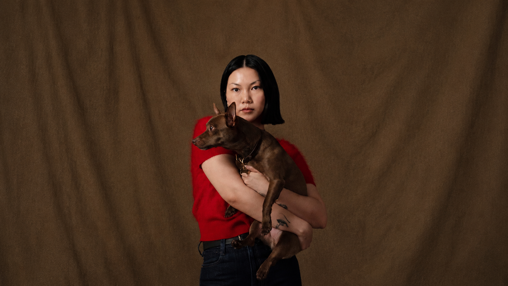 Alexandra Pauly holding her dog cam, founder of Biche dog care brand, red top brown background 