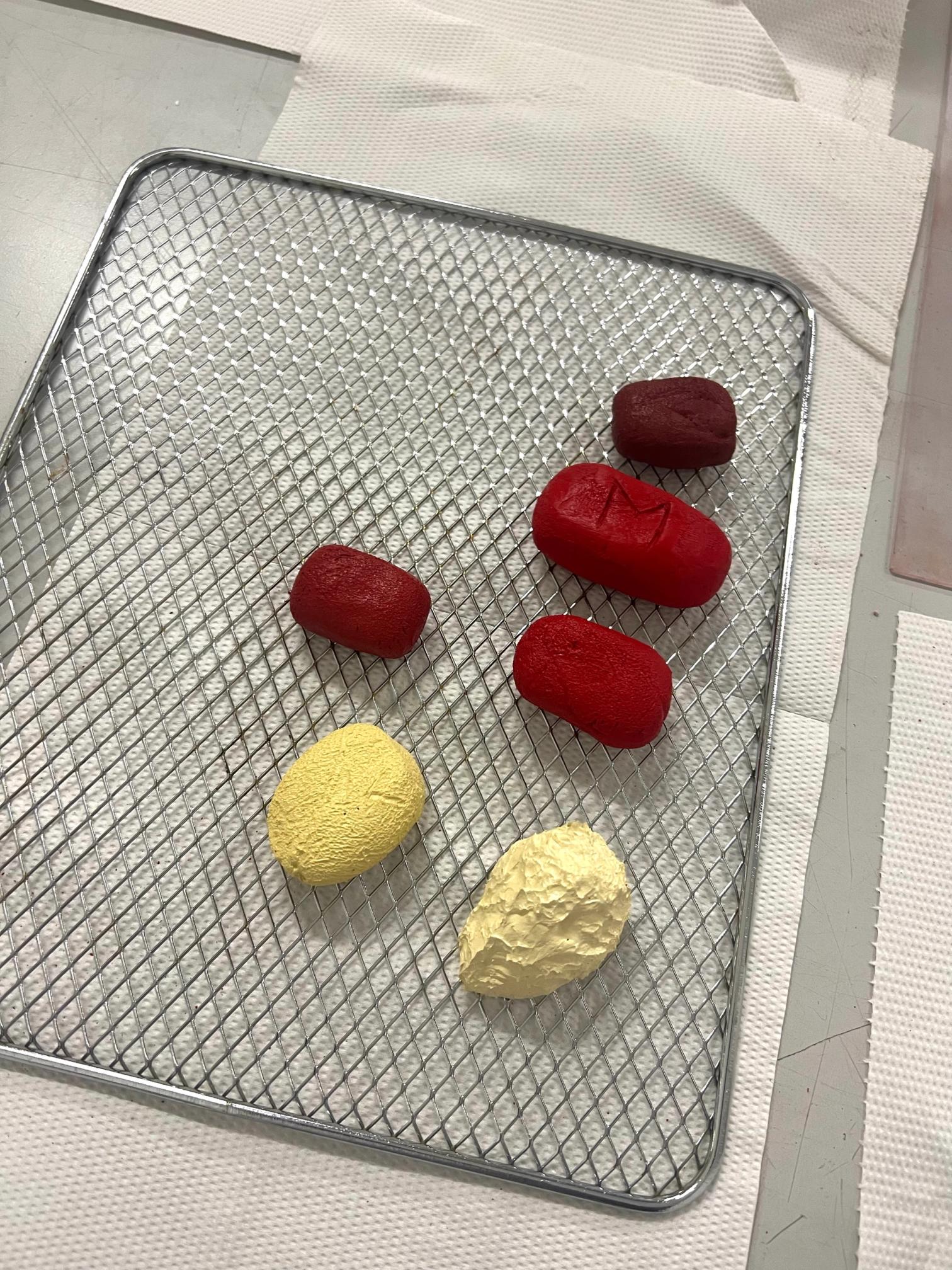 Five red and two textured yellow sculpted objects on a metal cooling rack.