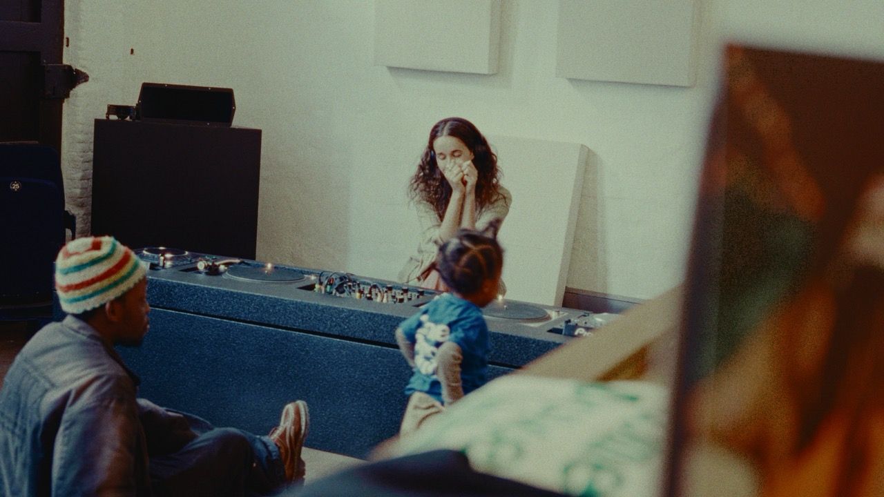 A man, child, and woman in a room with a DJ setup, the woman covering her mouth.