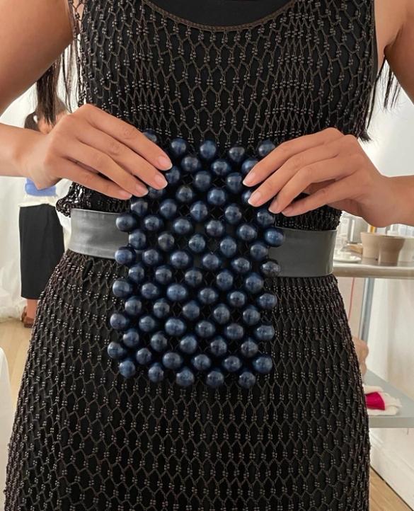 A person holds a rectangular dark blue beaded clutch over a black open-knit dress and belt.