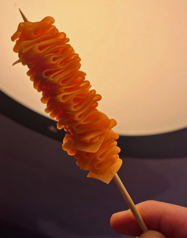 A hand holds a skewer of spiral-cut orange potato chips.