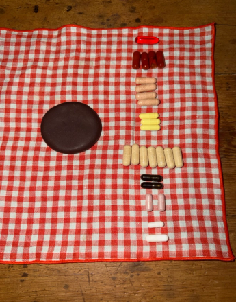 A dark chocolate disc next to several rows of colorful pills on a red and white checkered cloth.