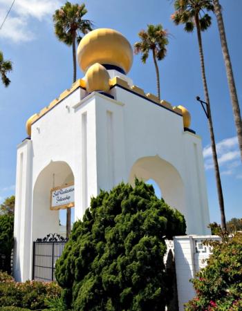 The Self-Realization Fellowship building, a white structure with golden domes and arches, surrounded by lush gardens and tall palm trees.