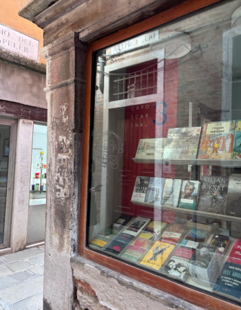 Old bookstore window displaying books, with street reflections.