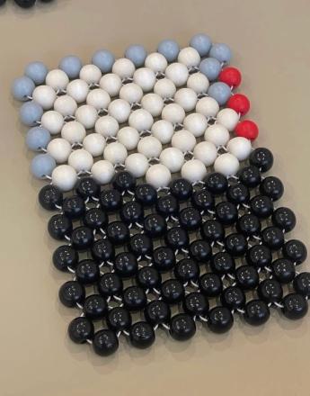 A beaded mat featuring a black bottom half, a wide white band, pale blue beads on the top left, and red beads on the top right.