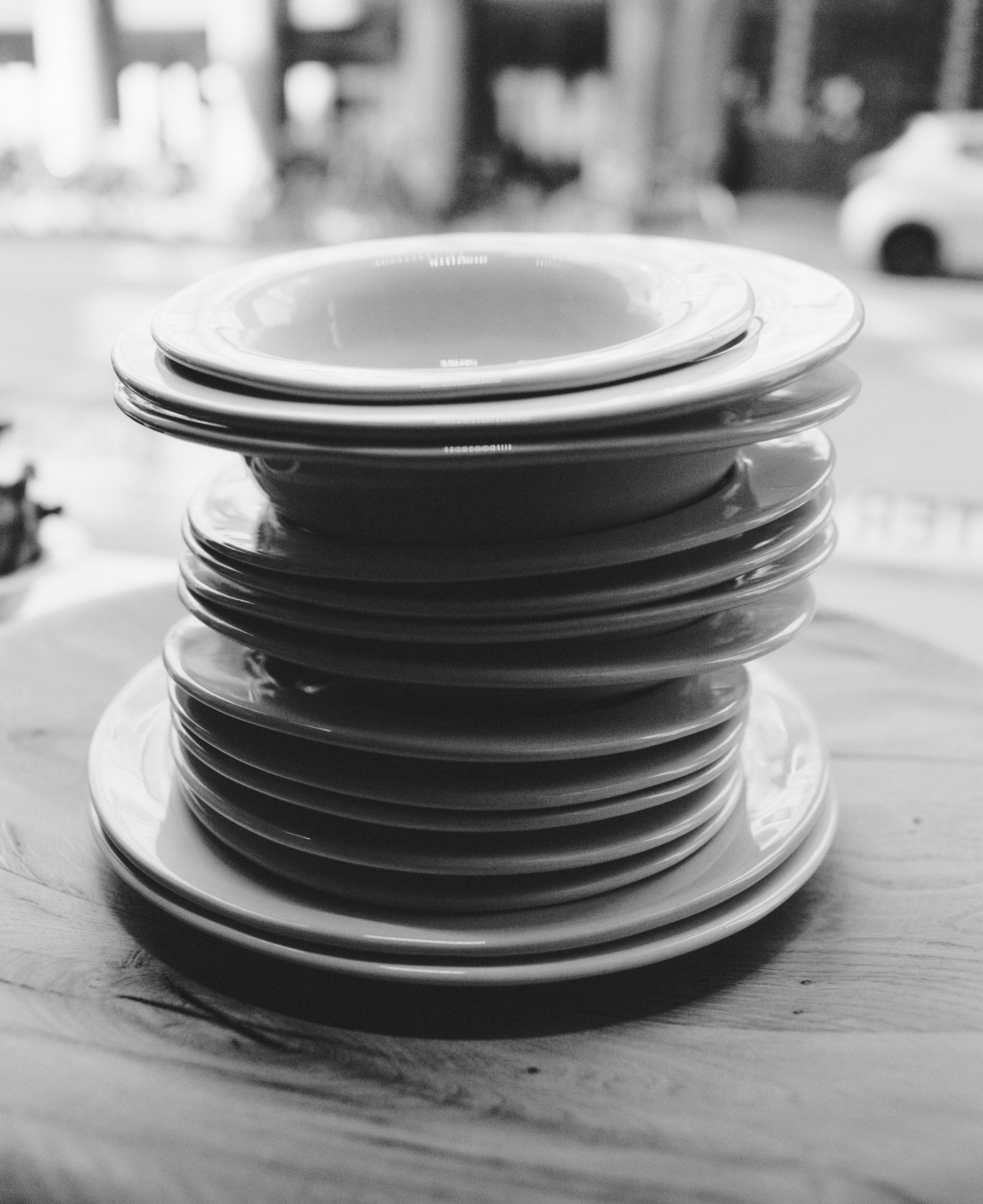 Black and white image of a tall stack of plates and bowls on a wooden table.