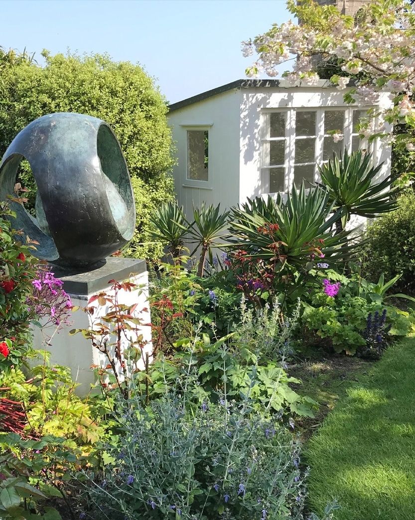 Bronze sculpture in a vibrant garden with a white studio and cherry blossoms.