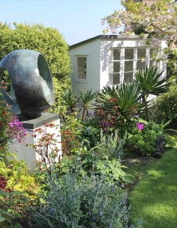 Bronze sculpture in a vibrant garden with a white studio and cherry blossoms.