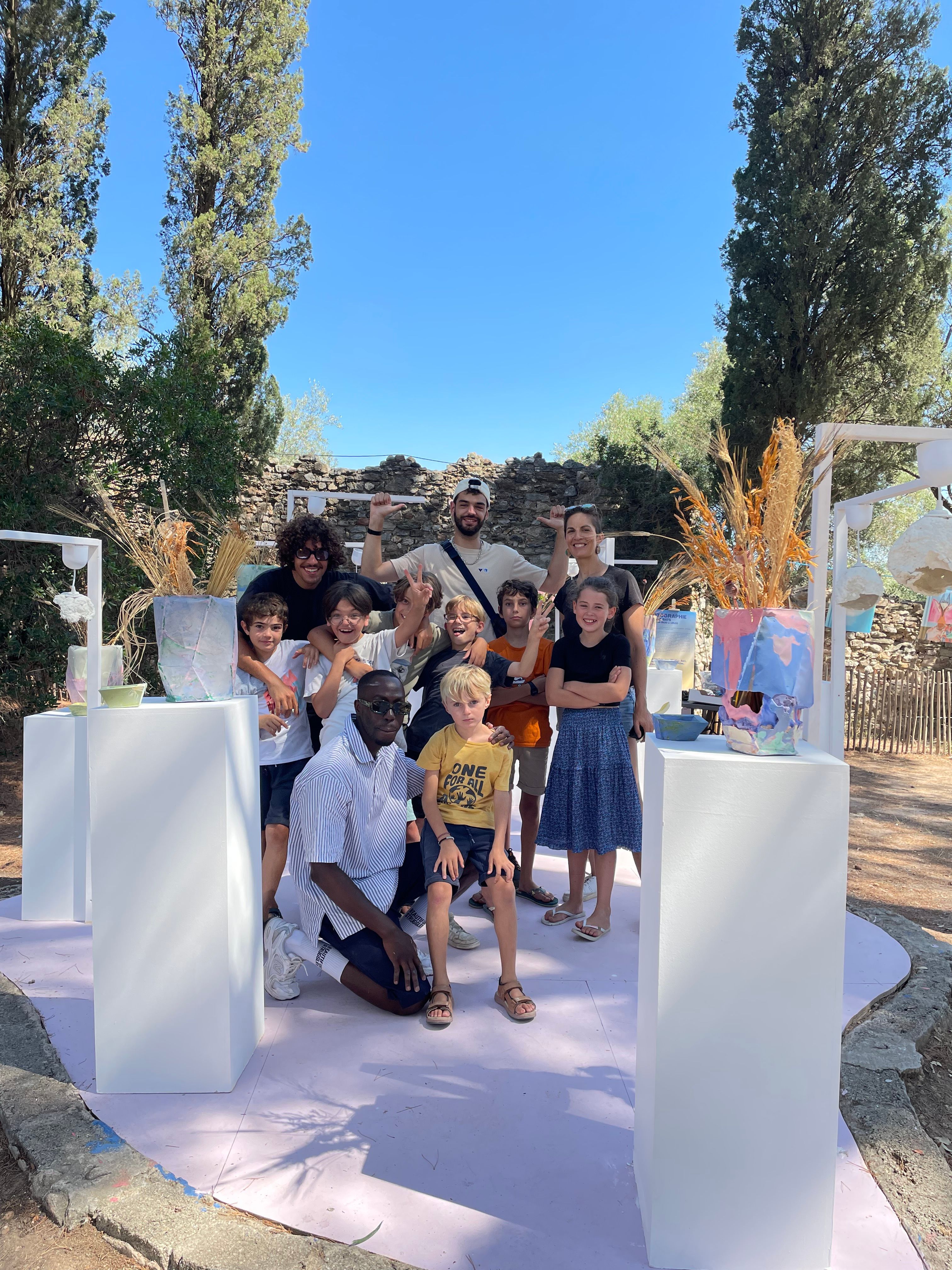 A diverse group of smiling adults and children pose outdoors with colorful artwork on white pedestals.