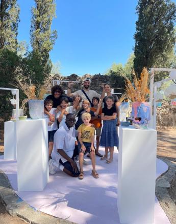 A diverse group of smiling adults and children pose outdoors with colorful artwork on white pedestals.