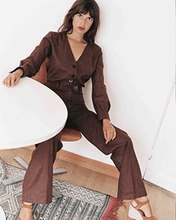 A woman in a dark brown matching top and wide-leg pants sits at a white table.