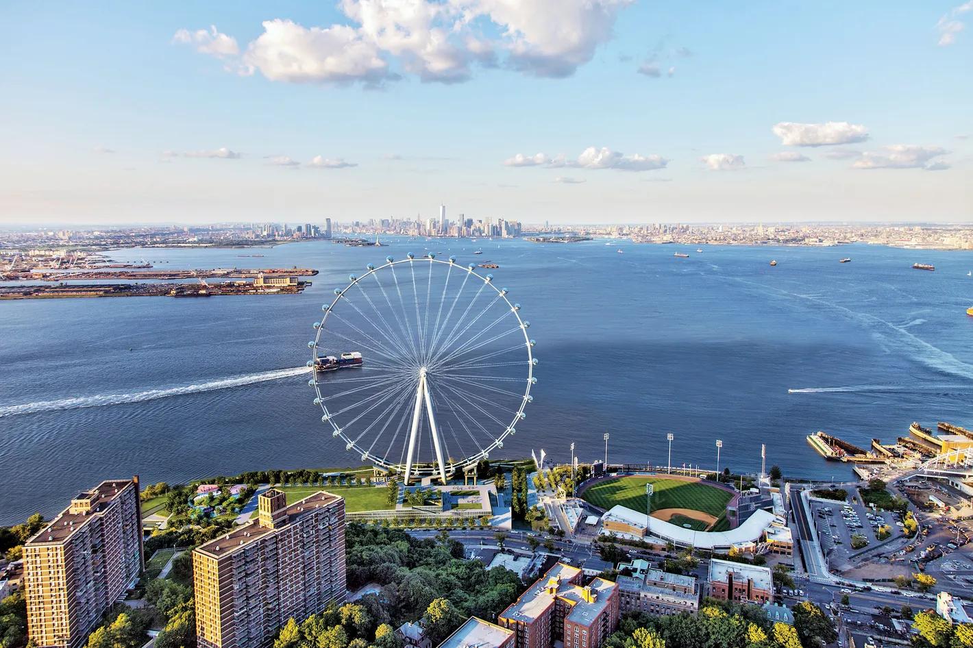 Aerial view of a large Ferris wheel on a waterfront with a baseball field, residential buildings, and the Manhattan skyline in the distance.