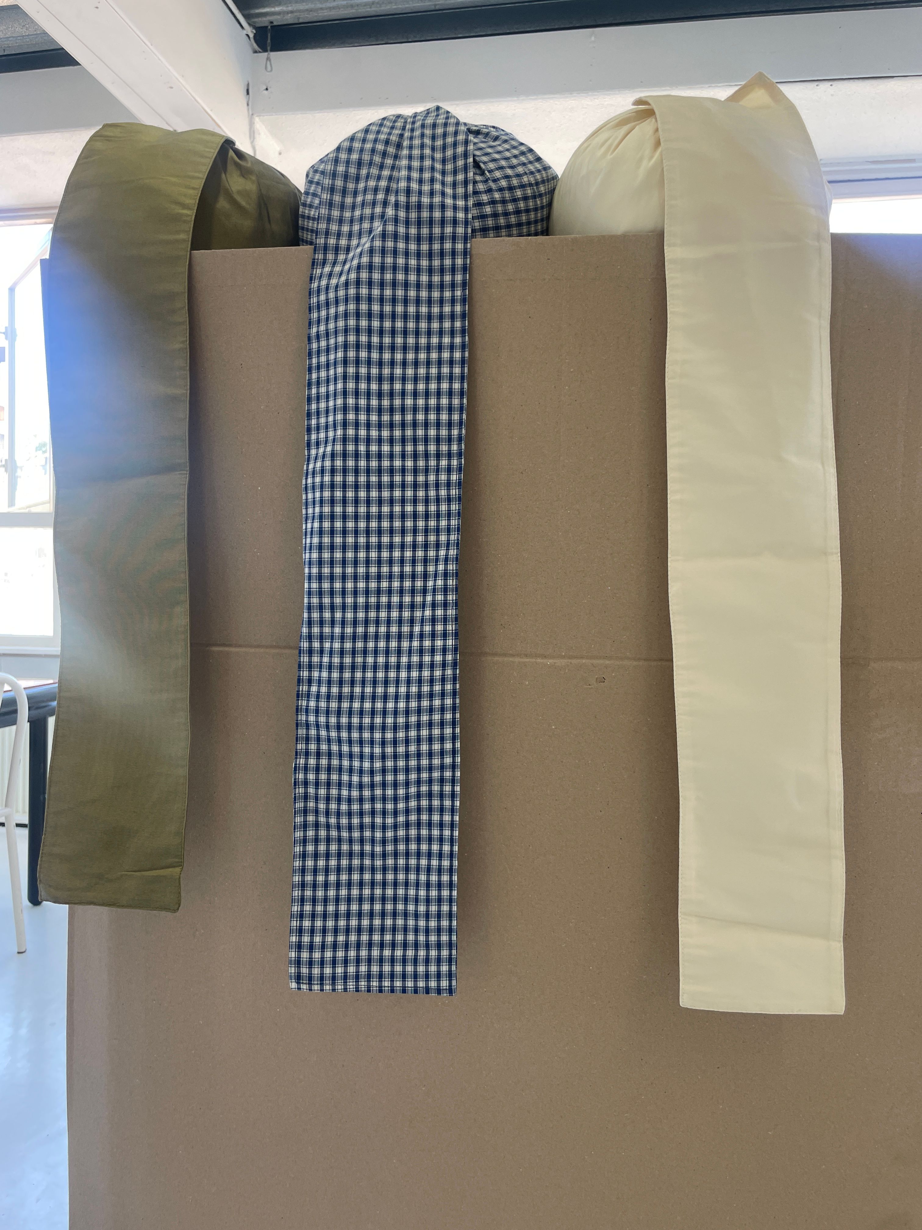 Three fabric swatches: olive green, blue gingham, and cream, draped over a brown box.