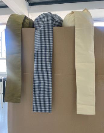 Three fabric swatches: olive green, blue gingham, and cream, draped over a brown box.