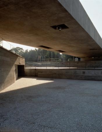 A wide concrete overhang above a large, paved plaza, with strong shadows and concrete walls.