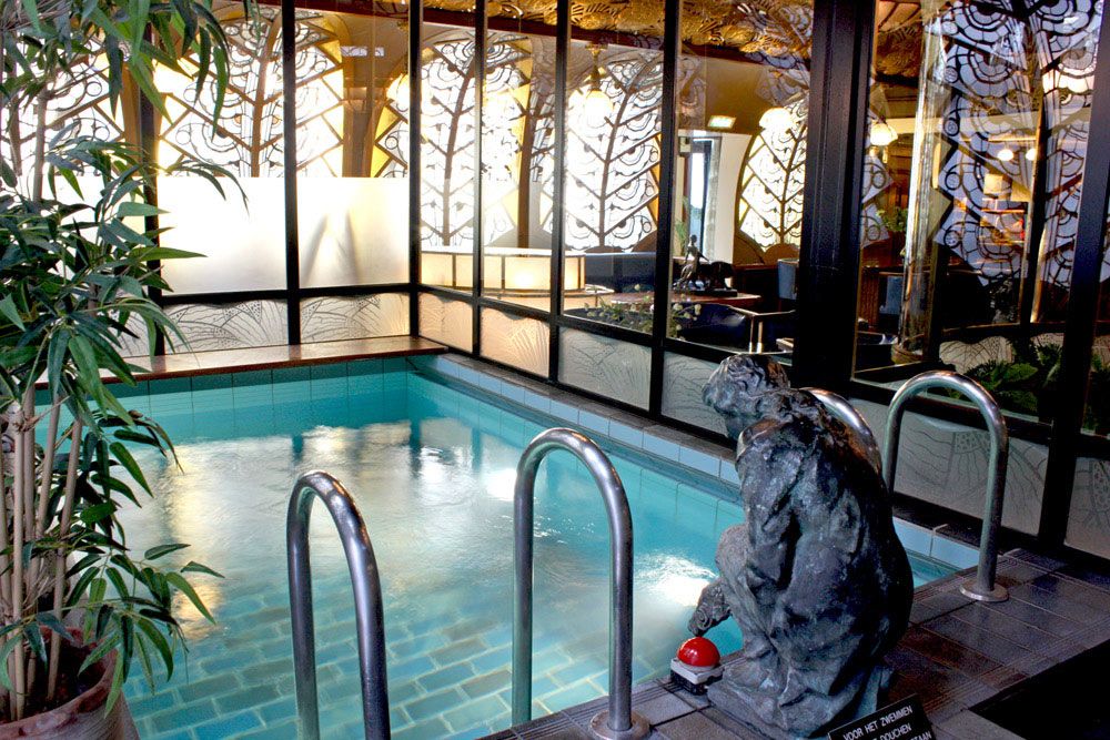 An indoor pool with a statue, surrounded by ornate, glowing stained glass panels and tiled surfaces.