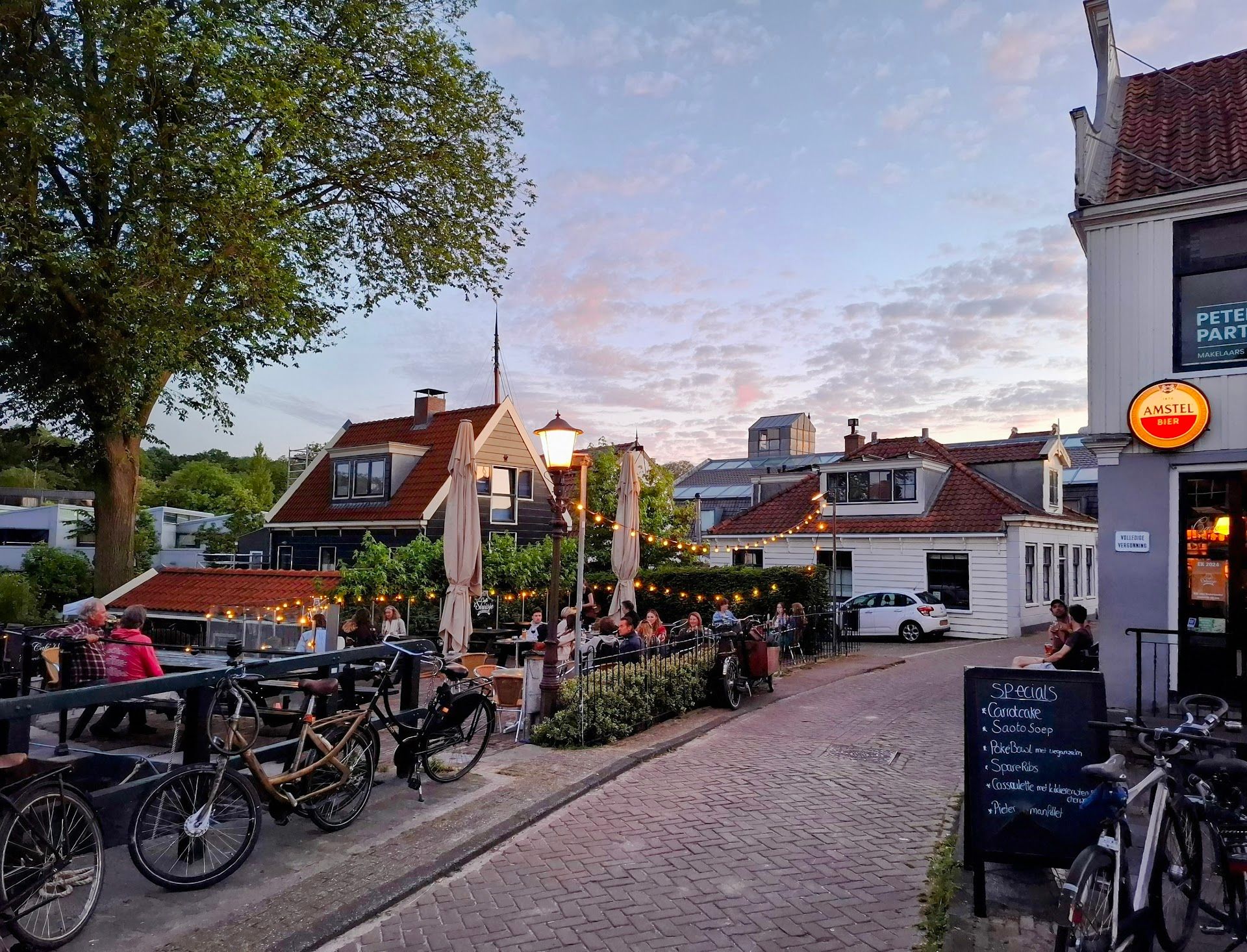 Outdoor cafe dining under string lights on a charming European street at dusk, with traditional buildings and parked bicycles.