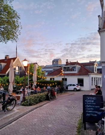 Outdoor cafe dining under string lights on a charming European street at dusk, with traditional buildings and parked bicycles.